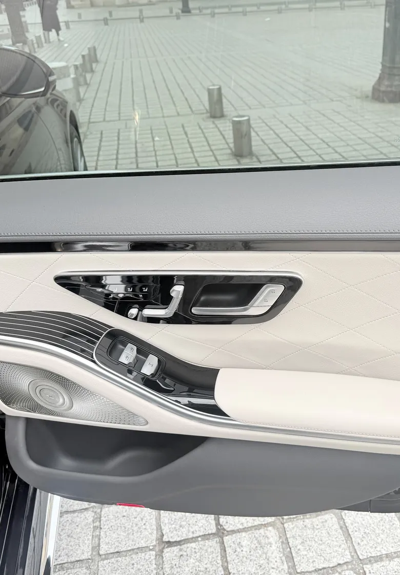 Ivory quilted leather door panel of a Mercedes S-Class, cobblestones through the window